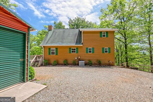 back of property featuring fence, gravel driveway, cooling unit, roof with shingles, and a chimney