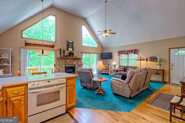 kitchen with ceiling fan, electric range, a stone fireplace, high vaulted ceiling, and light wood-style flooring