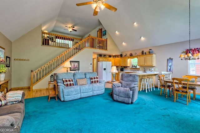 carpeted living room with stairway, high vaulted ceiling, baseboards, and ceiling fan with notable chandelier