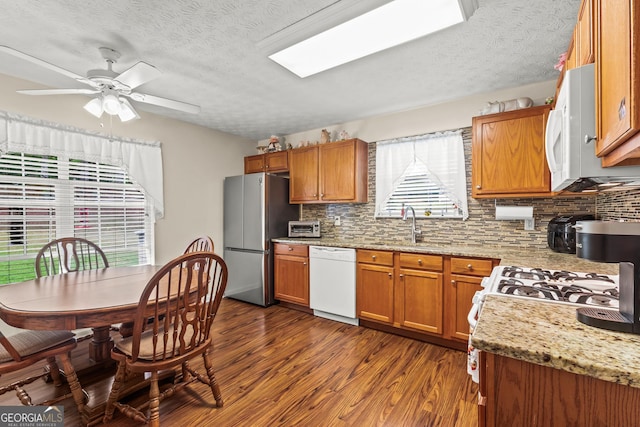 kitchen with white appliances, dark wood-style flooring, brown cabinetry, and a sink