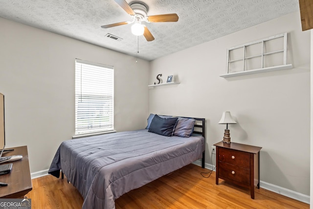 bedroom featuring a ceiling fan, a textured ceiling, visible vents, wood finished floors, and baseboards