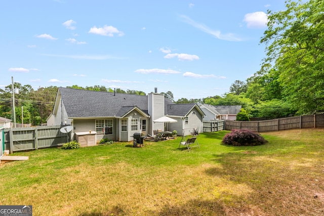 rear view of property featuring a fenced backyard, a chimney, and a yard