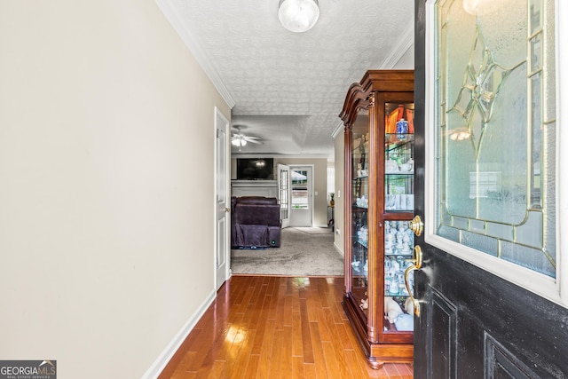 hallway featuring crown molding, a textured ceiling, baseboards, and wood finished floors