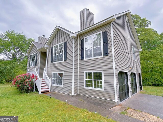view of side of property with a lawn, a chimney, a garage, and aphalt driveway