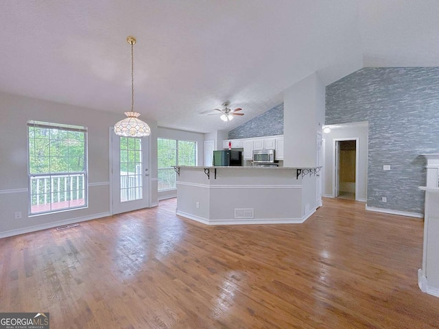 unfurnished living room with ceiling fan, light wood-style floors, high vaulted ceiling, baseboards, and visible vents