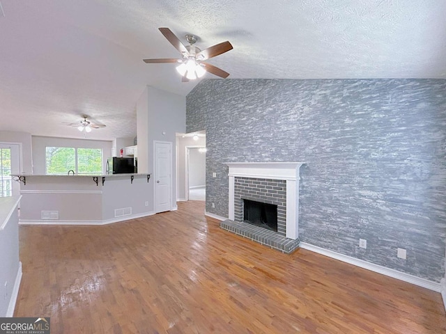unfurnished living room with a textured ceiling, ceiling fan, vaulted ceiling, and wood finished floors