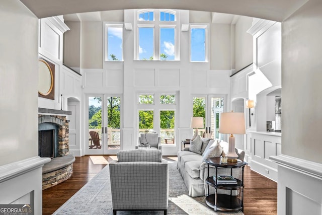 living room featuring french doors, a fireplace, dark wood-style floors, a high ceiling, and a decorative wall