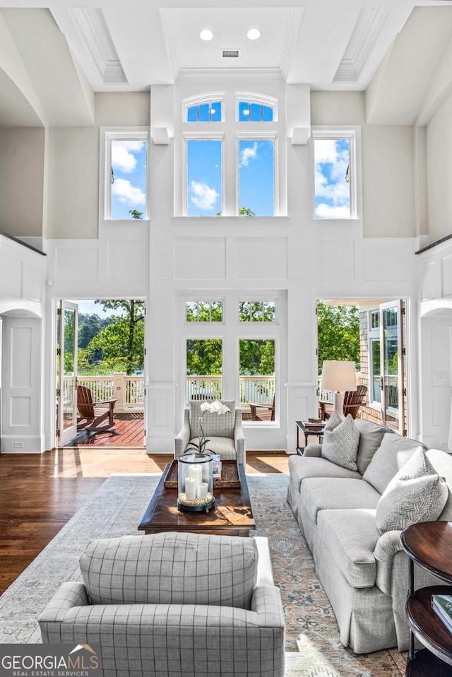 living area featuring ornamental molding, a decorative wall, wood finished floors, and a towering ceiling