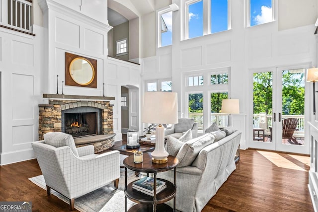 living area with a towering ceiling, a stone fireplace, dark wood-type flooring, and a decorative wall