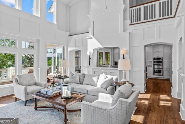living room featuring arched walkways, a decorative wall, dark wood-style floors, and a towering ceiling