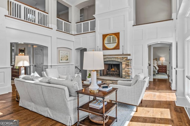living room featuring arched walkways, a decorative wall, a stone fireplace, and a towering ceiling