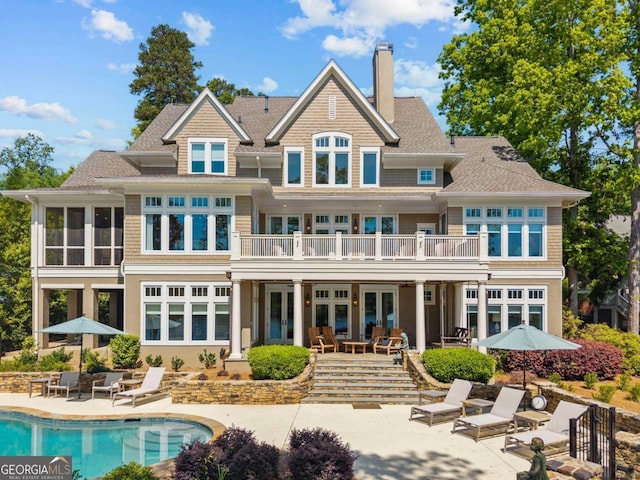rear view of house featuring roof with shingles, french doors, a chimney, a fenced in pool, and a patio area