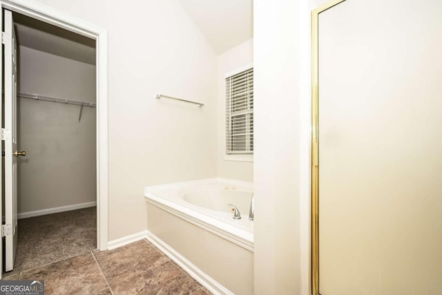 bathroom featuring a walk in closet, baseboards, and a garden tub