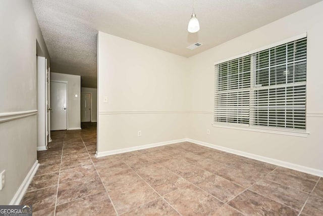tiled spare room featuring baseboards, a textured ceiling, and visible vents