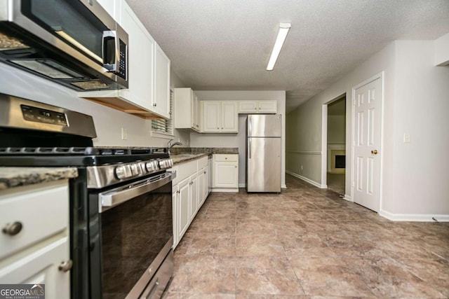 kitchen with a textured ceiling, appliances with stainless steel finishes, a sink, baseboards, and white cabinetry