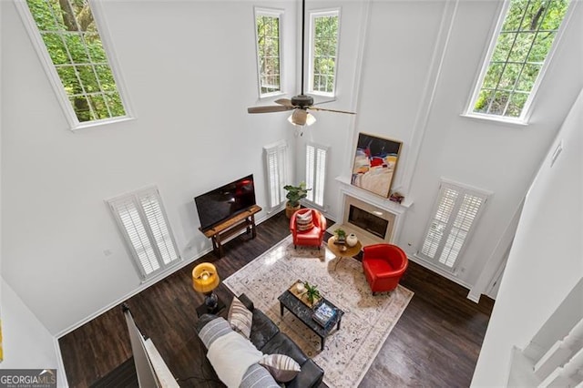living area with a high ceiling, ceiling fan, wood finished floors, and a fireplace