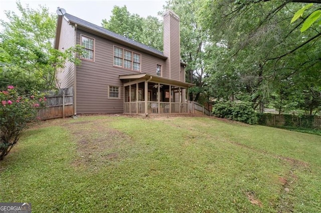 back of property featuring a fenced backyard, a sunroom, a chimney, and a yard