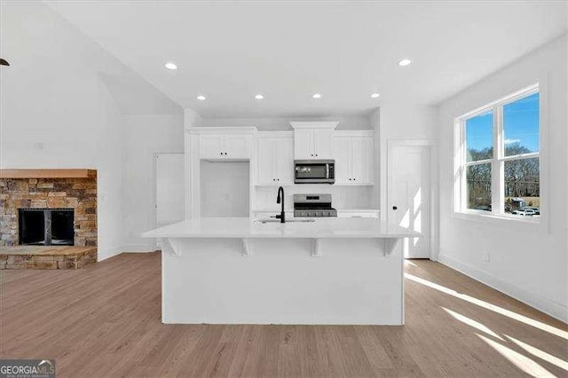 kitchen featuring a kitchen island with sink, baseboards, white cabinets, a sink, and appliances with stainless steel finishes