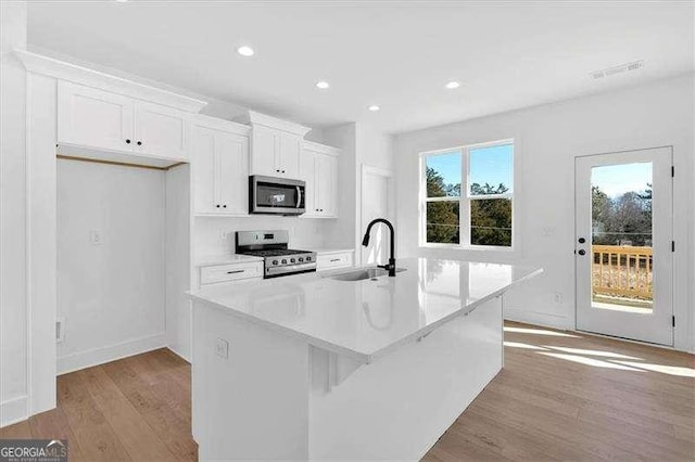 kitchen featuring a sink, light wood-style flooring, stainless steel appliances, white cabinetry, and a center island with sink
