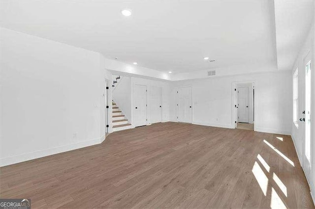 unfurnished living room with stairs, wood finished floors, baseboards, recessed lighting, and a tray ceiling