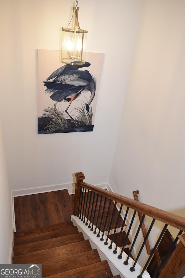 stairway with an inviting chandelier, baseboards, and wood finished floors