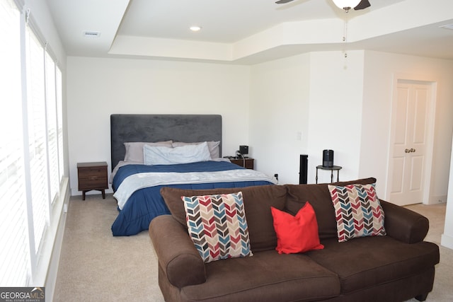 bedroom with light colored carpet, a raised ceiling, ceiling fan, and visible vents