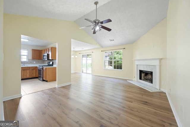 unfurnished living room with ceiling fan, a high end fireplace, light wood-style flooring, a textured ceiling, and baseboards