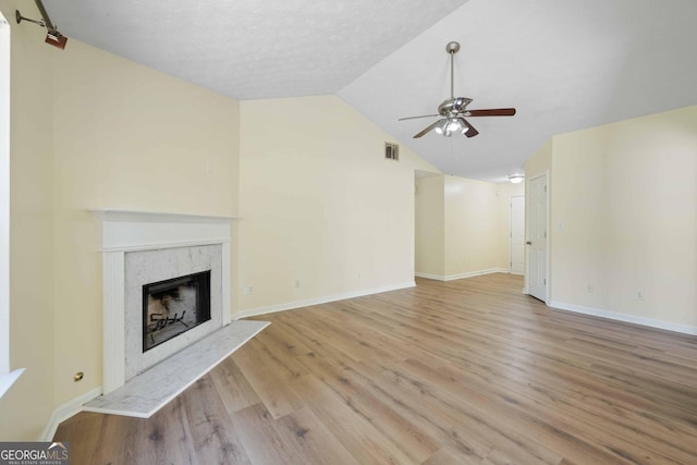 unfurnished living room featuring ceiling fan, vaulted ceiling, a fireplace, light wood-style floors, and baseboards