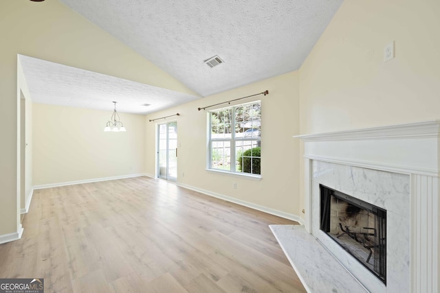 unfurnished living room featuring a high end fireplace, lofted ceiling, a textured ceiling, wood finished floors, and a chandelier