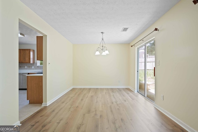 unfurnished dining area featuring light wood-style flooring, a chandelier, a textured ceiling, and baseboards
