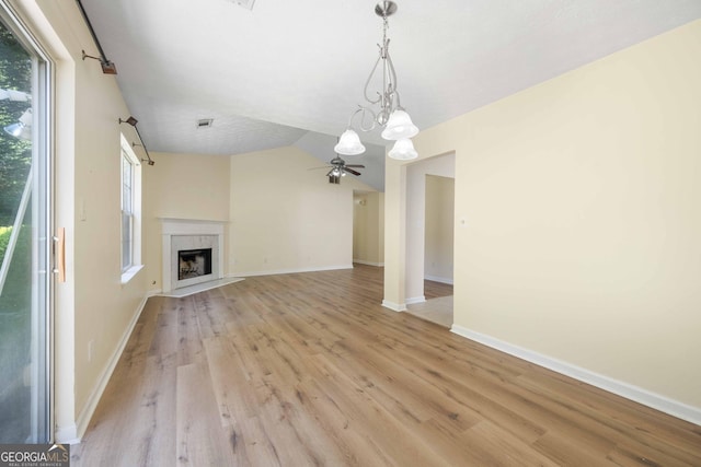 unfurnished living room with light wood-style flooring, a chandelier, ceiling fan, a fireplace with flush hearth, and baseboards