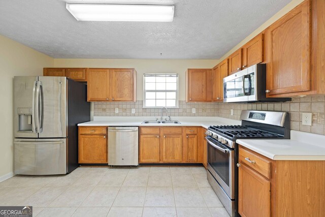 kitchen with stainless steel appliances, a sink, tasteful backsplash, light countertops, and a textured ceiling