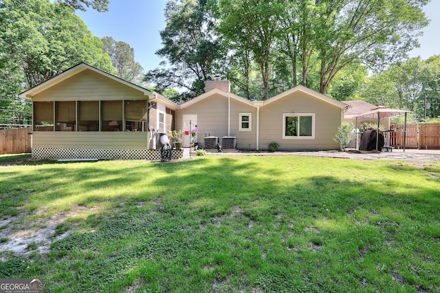 rear view of property with fence, a sunroom, central AC unit, a chimney, and a lawn