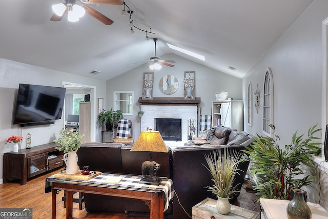 living area featuring visible vents, wood finished floors, a fireplace, vaulted ceiling with skylight, and a ceiling fan