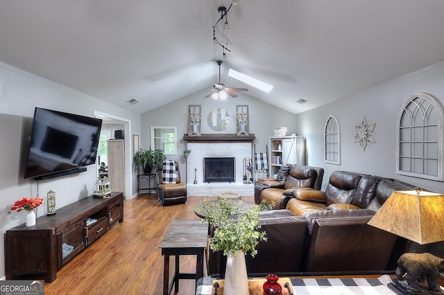 living area with ceiling fan, track lighting, a fireplace, wood finished floors, and vaulted ceiling