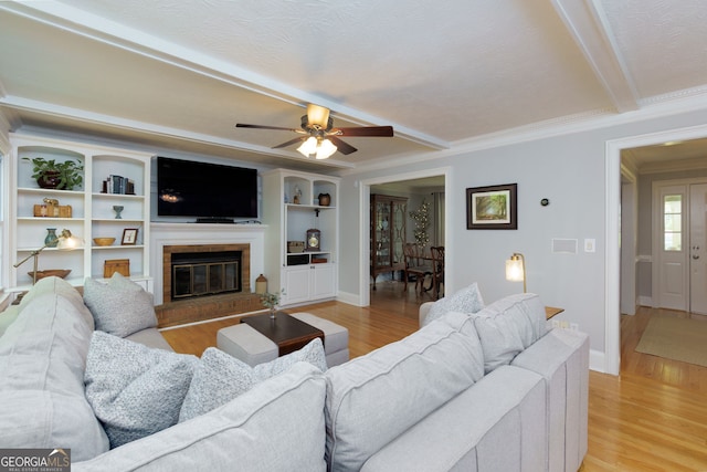 living area with crown molding, light wood-style flooring, a brick fireplace, and beamed ceiling