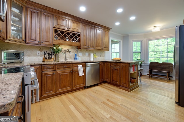 kitchen with a sink, light wood-style floors, stainless steel appliances, a toaster, and ornamental molding