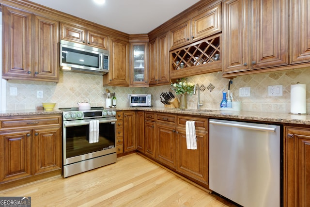 kitchen with appliances with stainless steel finishes, light wood finished floors, brown cabinets, and light stone counters