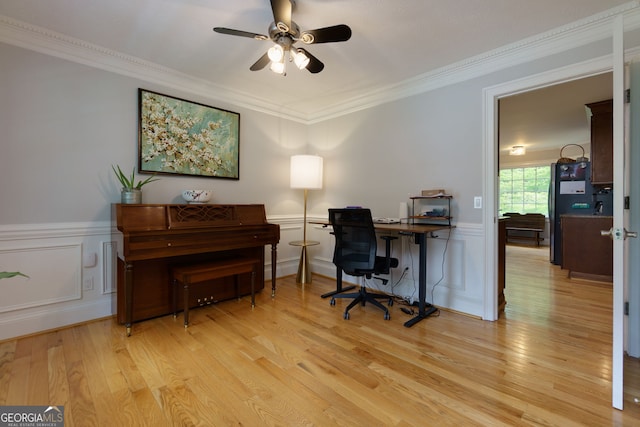 office area with ornamental molding, a decorative wall, ceiling fan, a wainscoted wall, and light wood finished floors