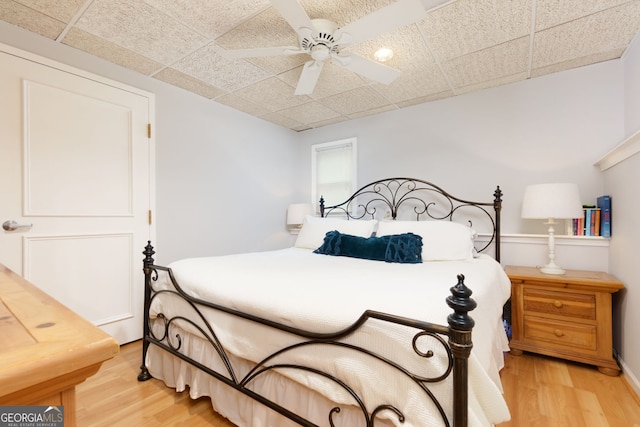 bedroom with a paneled ceiling, a ceiling fan, and light wood-style flooring