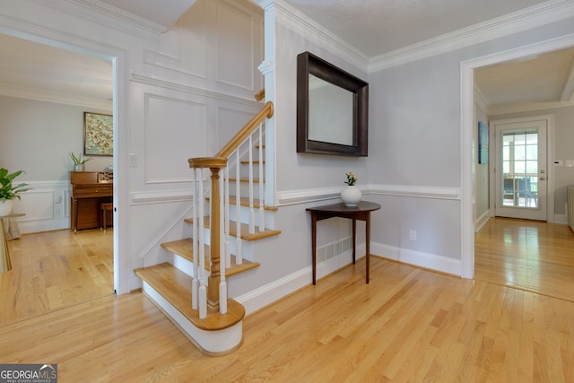 stairway with crown molding, a decorative wall, wood finished floors, and visible vents