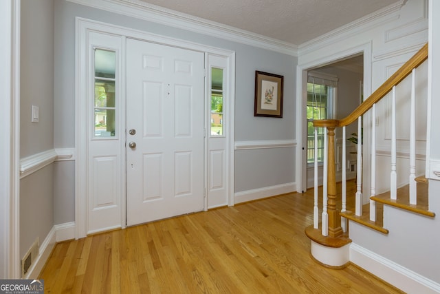 foyer featuring visible vents, light wood-type flooring, stairway, baseboards, and ornamental molding