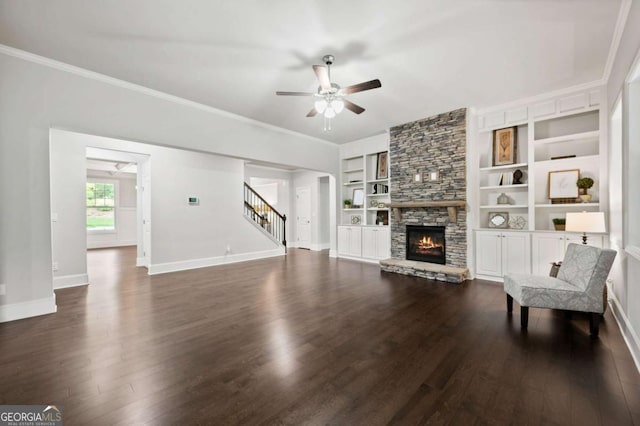 unfurnished living room with ceiling fan, dark wood finished floors, a stone fireplace, stairs, and baseboards
