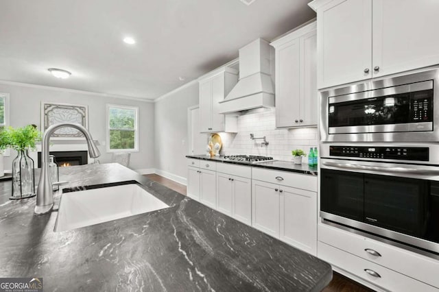 kitchen featuring tasteful backsplash, a sink, custom exhaust hood, ornamental molding, and stainless steel appliances