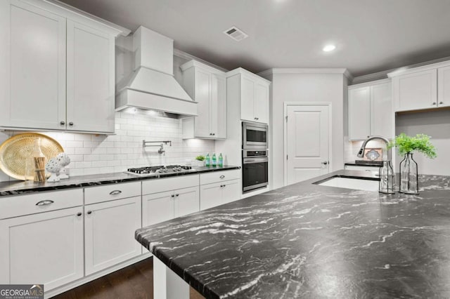 kitchen with crown molding, visible vents, custom range hood, a sink, and appliances with stainless steel finishes