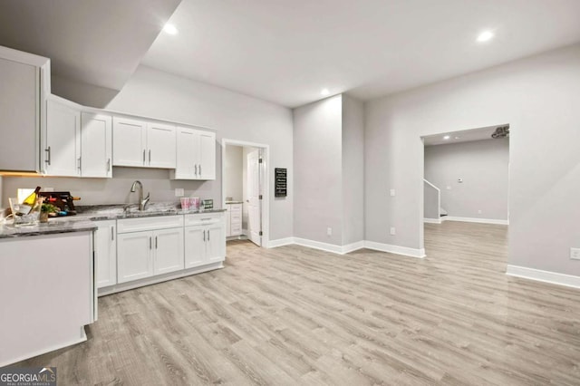 kitchen with light wood-style floors, a sink, white cabinetry, and baseboards