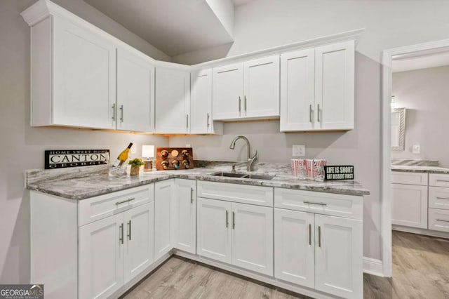 kitchen with light stone counters, a sink, light wood-style flooring, and white cabinetry