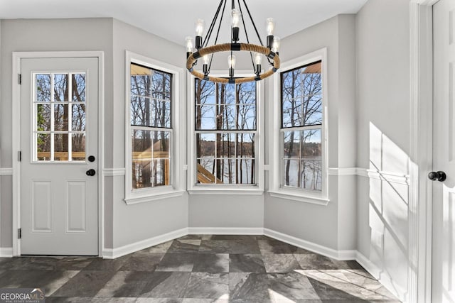 unfurnished dining area featuring stone finish flooring, baseboards, a chandelier, and a healthy amount of sunlight