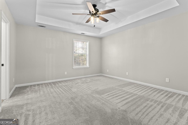 empty room featuring ceiling fan, visible vents, a raised ceiling, baseboards, and carpet flooring