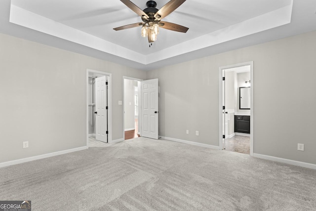 unfurnished bedroom with light colored carpet, a raised ceiling, ensuite bathroom, and baseboards
